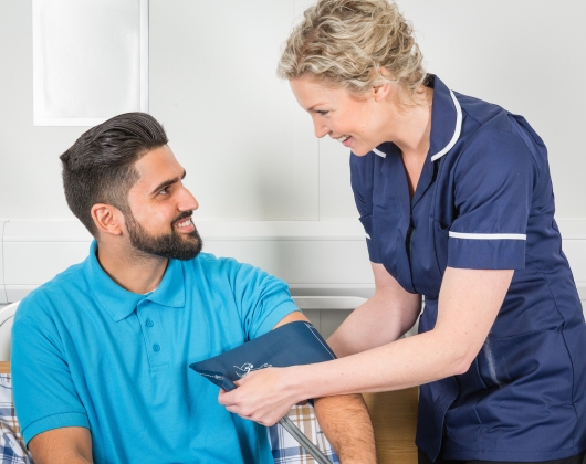 Nurse in blue scrubs taking blood pressure of man sitting in hospital bed