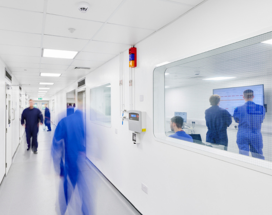 People walking through a hallway and working in a pharmaceutical manufacturing setting
