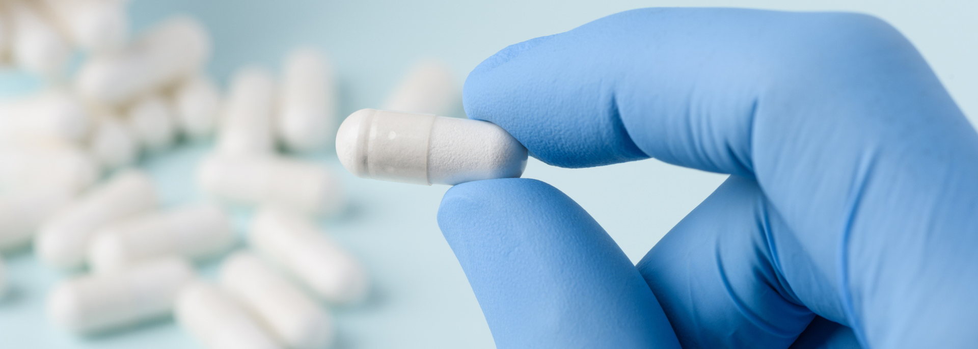Gloved hand holding white pill