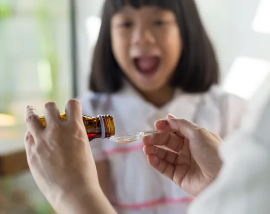 Hands of mom pouring cough syrup medicine into clear spoon for young daughter