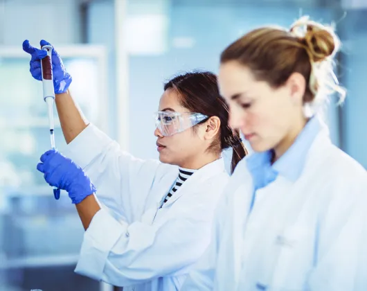 Two women in lab jackets, blue gloves in the laboratory