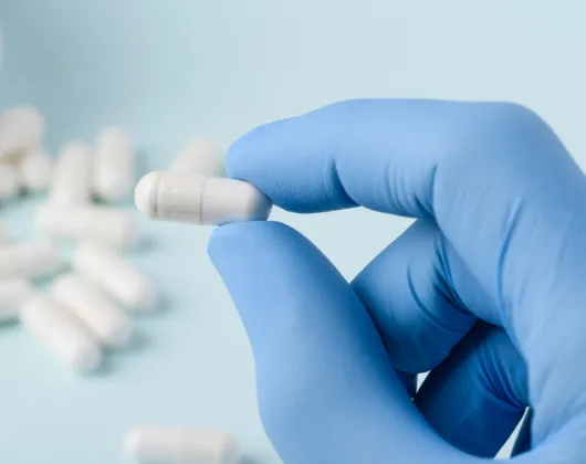 Blue gloves holding a white pill